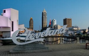 Picture of a large white sign that says "Cleveland" set against Lake Erie and the Cleveland skyline